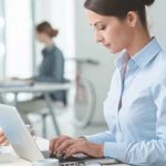 A businesswoman uses a laptop for vet compliance tasks in a modern office.