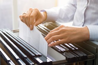 Hands sort documents in a filing cabinet, highlighting the importance of vet compliance.